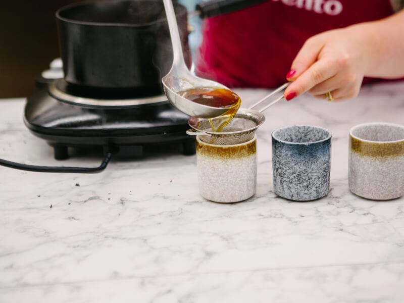Close up of a person pouring tea from a ladle into a row of Chinese tea cups